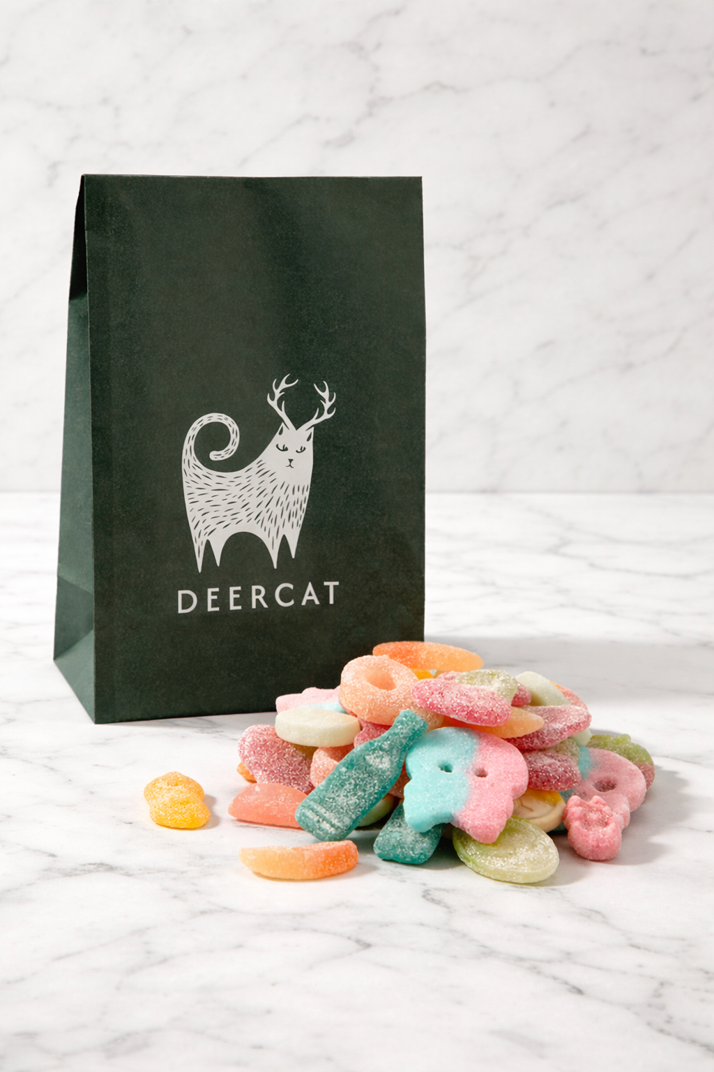 Black Deercat paper bag next to a pile of colorful sugar-coated gummy candies on white marble surface