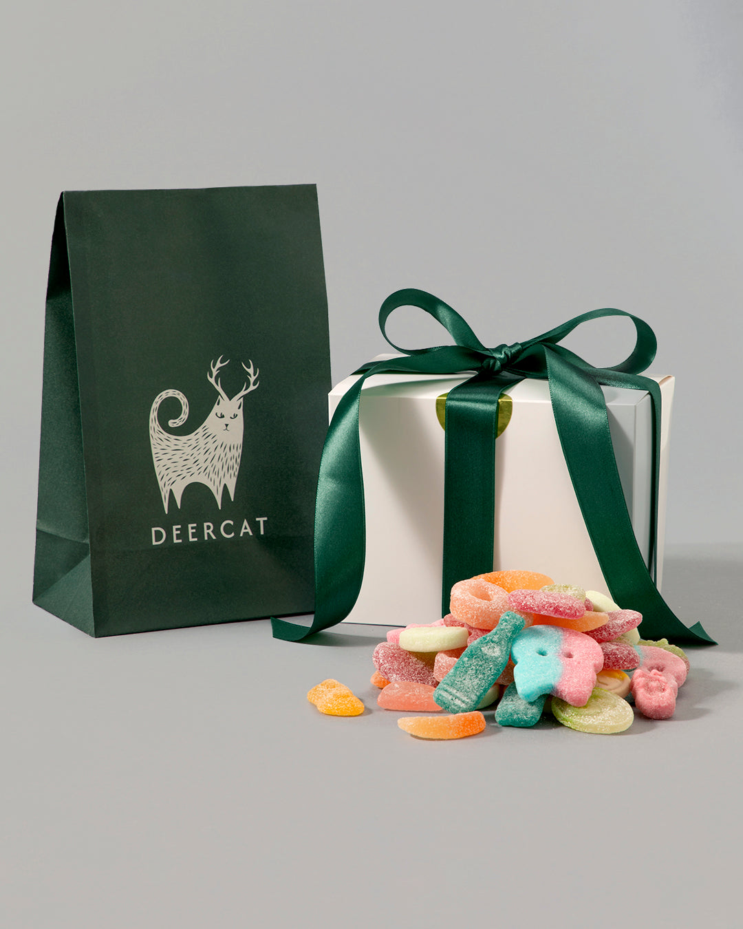 Assorted colorful vegan candy mix spilling in front of a white gift box with green ribbon and dark green Deercat bag