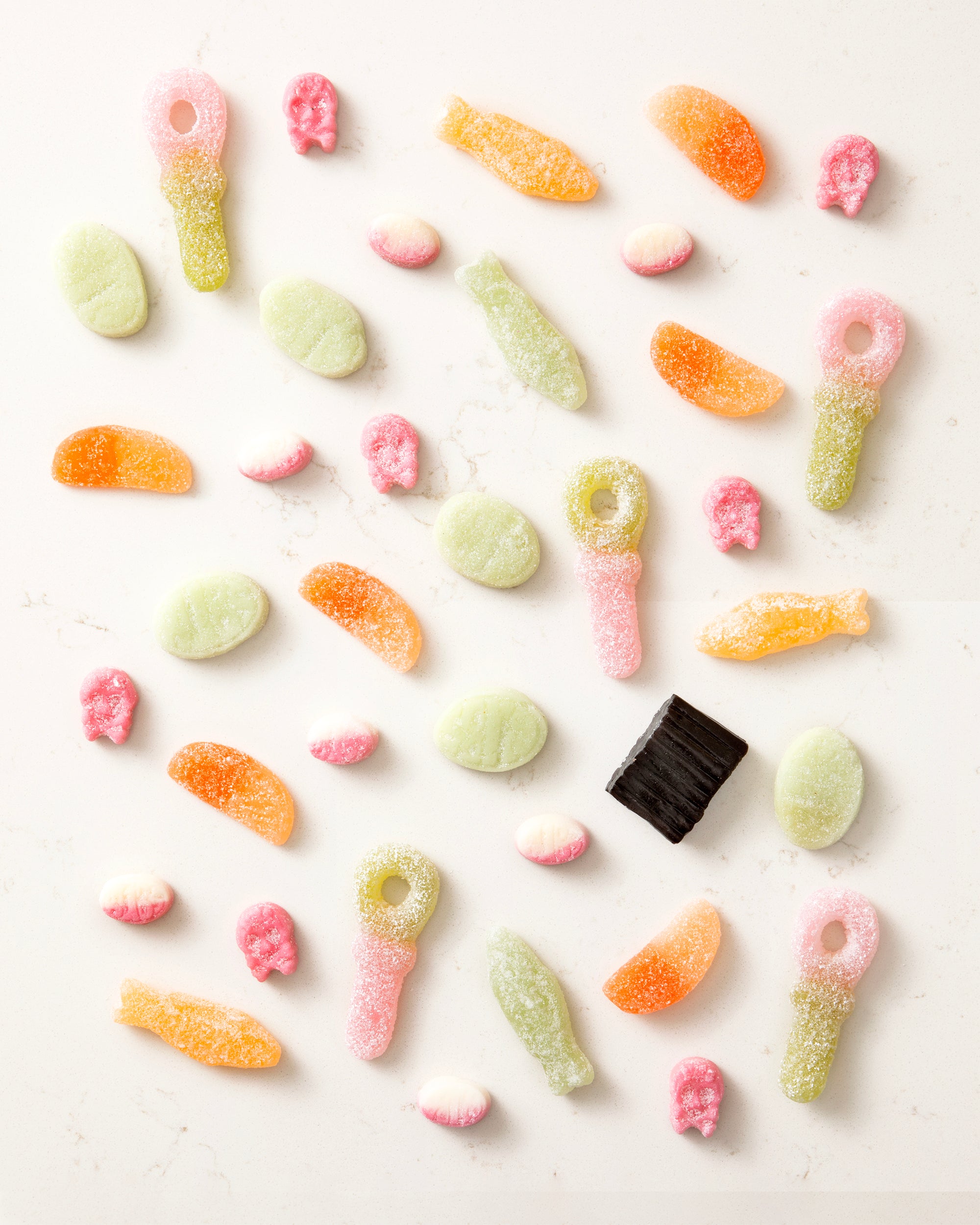 Assorted colorful vegan candy mix with gummy keys, fish shapes, skulls, and sugar-coated slices scattered on a white surface