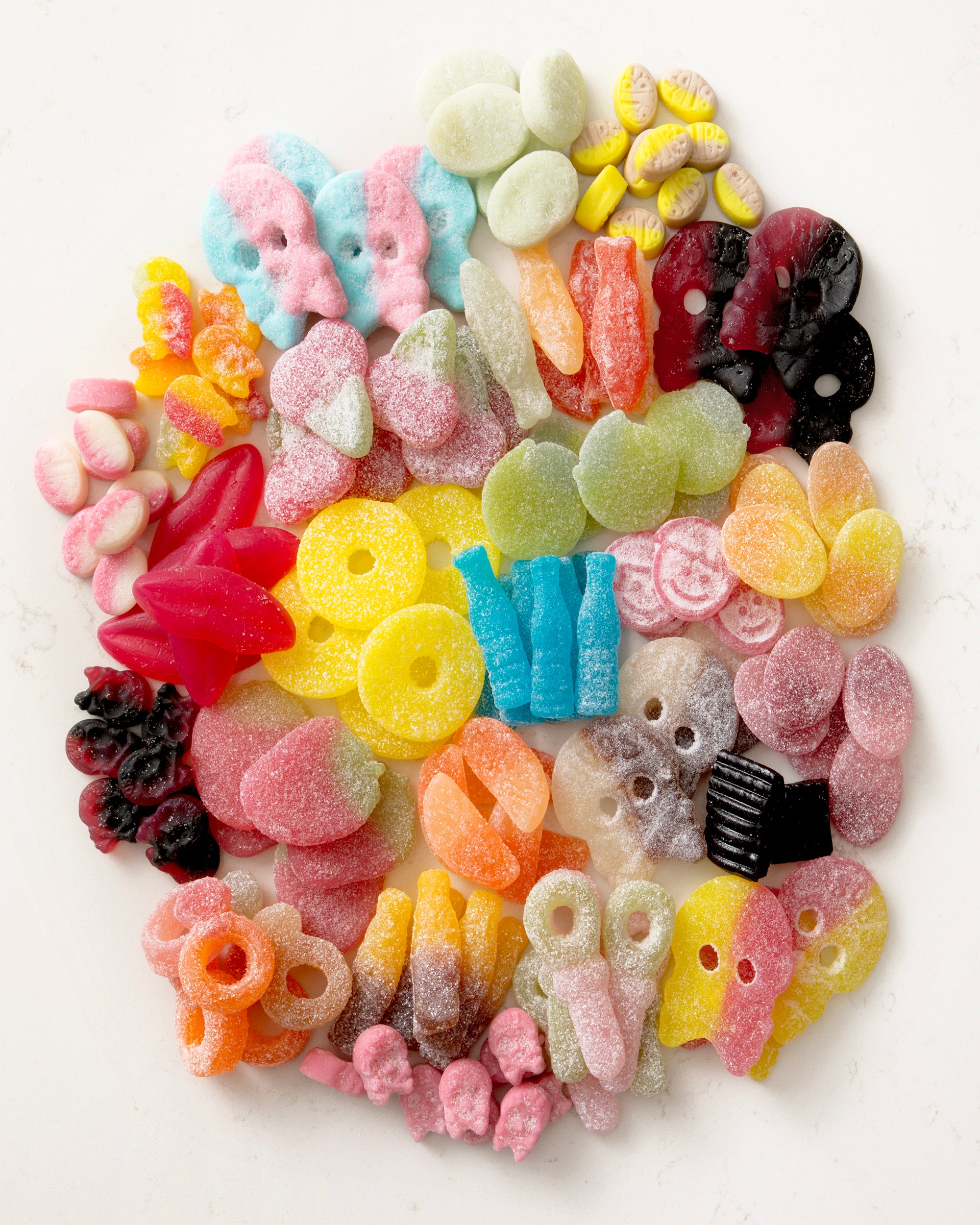 Assorted colorful vegan candy mix with various shapes and sugar coatings on a white background