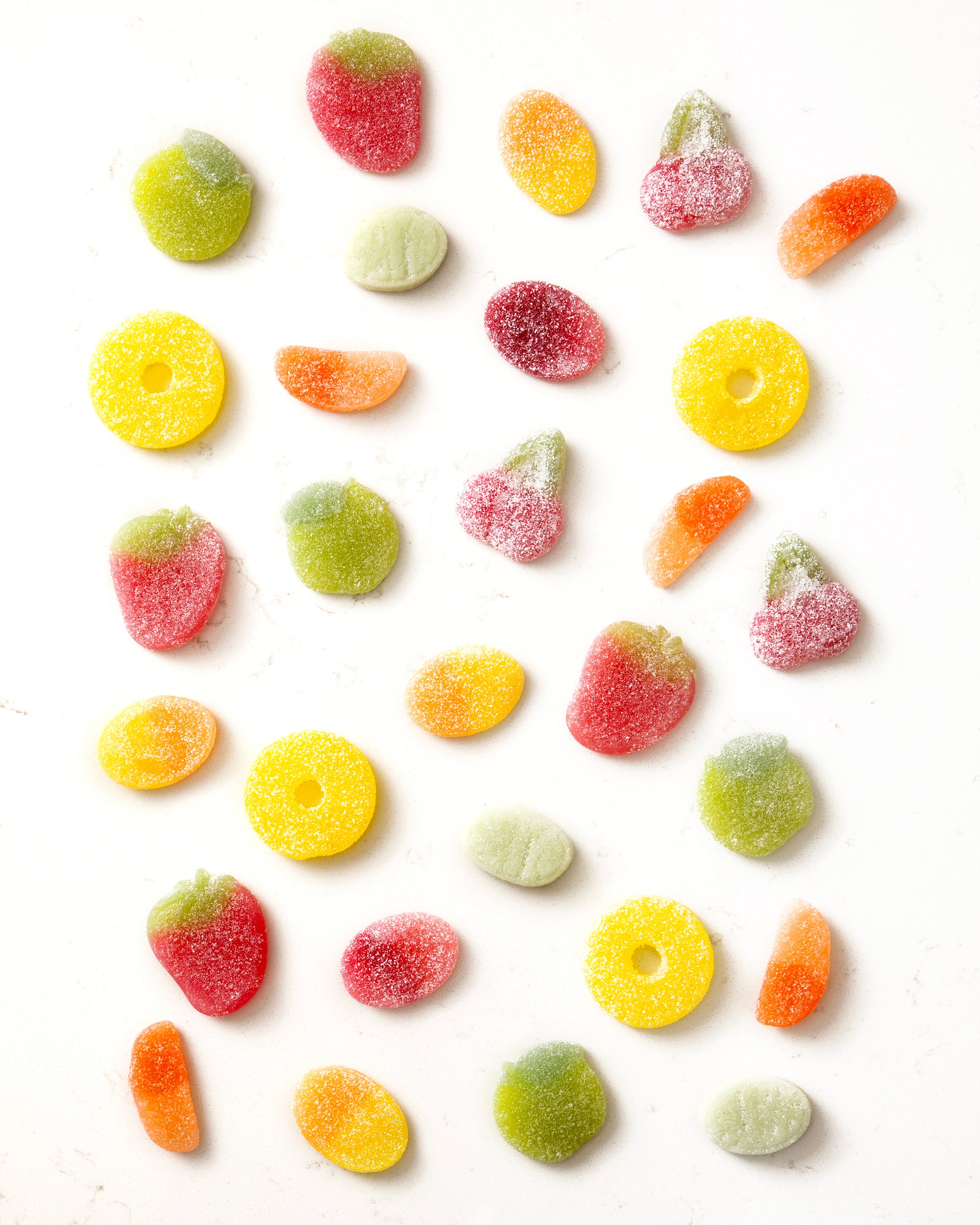 Colorful vegan sugar-coated gummy candies shaped like fruits scattered on a white background
