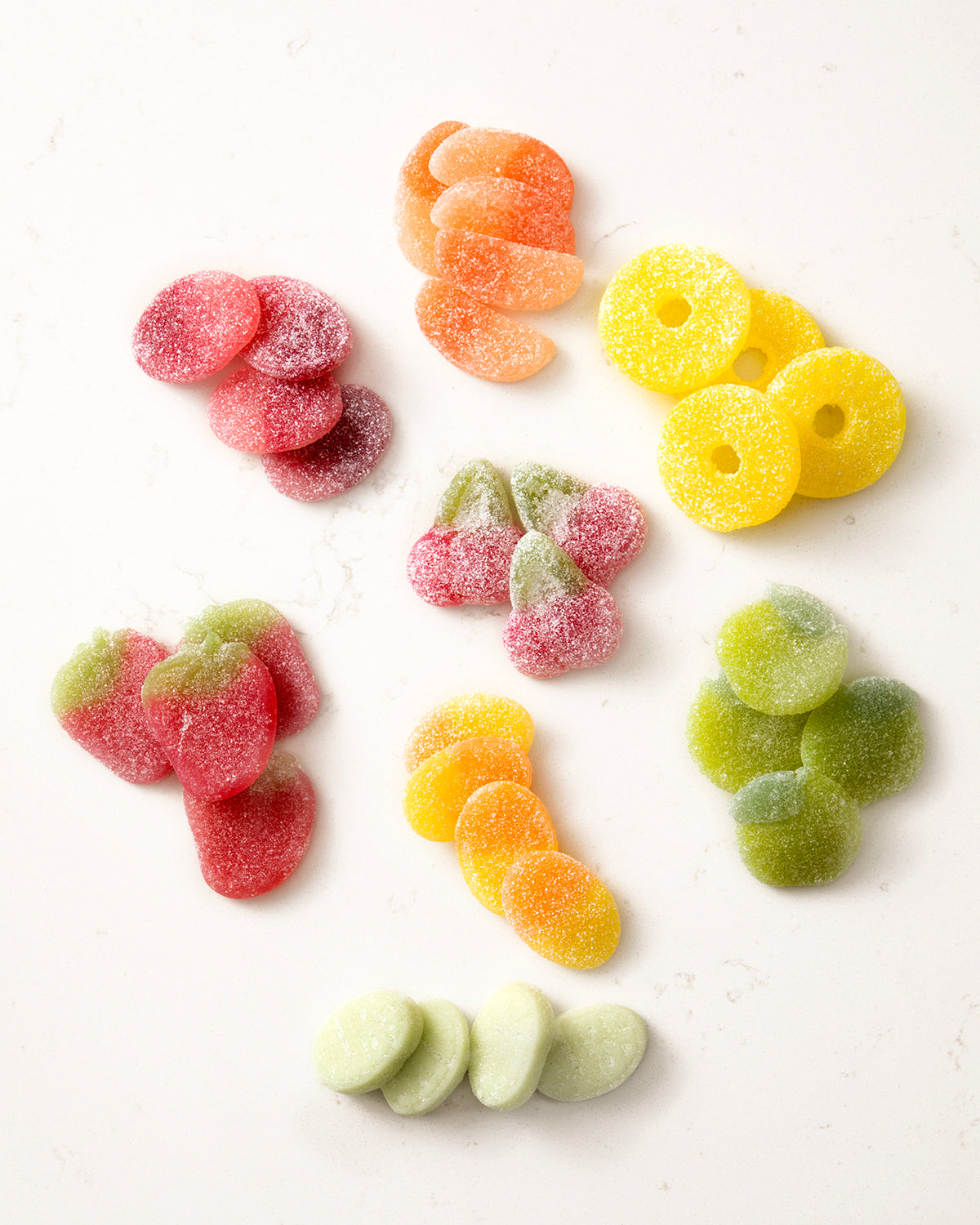 Assorted colorful vegan candy mixes coated in sugar, including rings, slices, and berry shapes on a white background