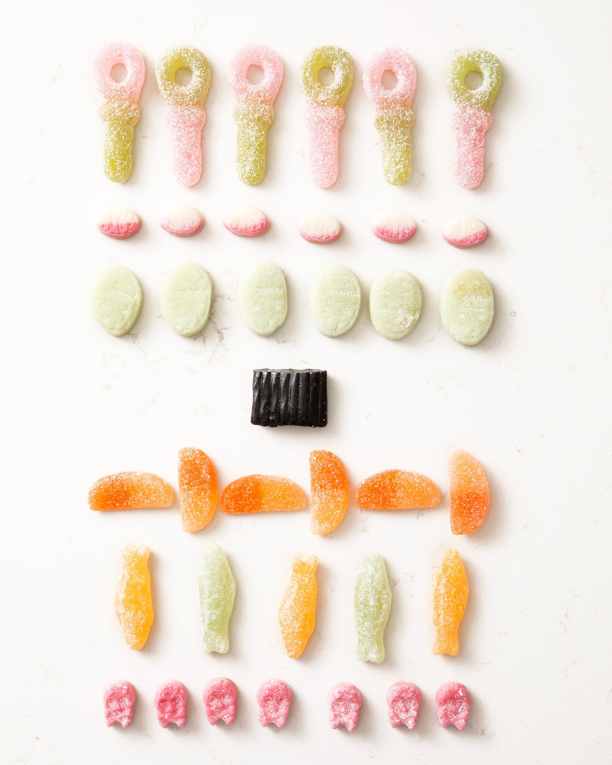 Rows of colorful vegan gummy candies arranged neatly on a white background in varied shapes and flavors