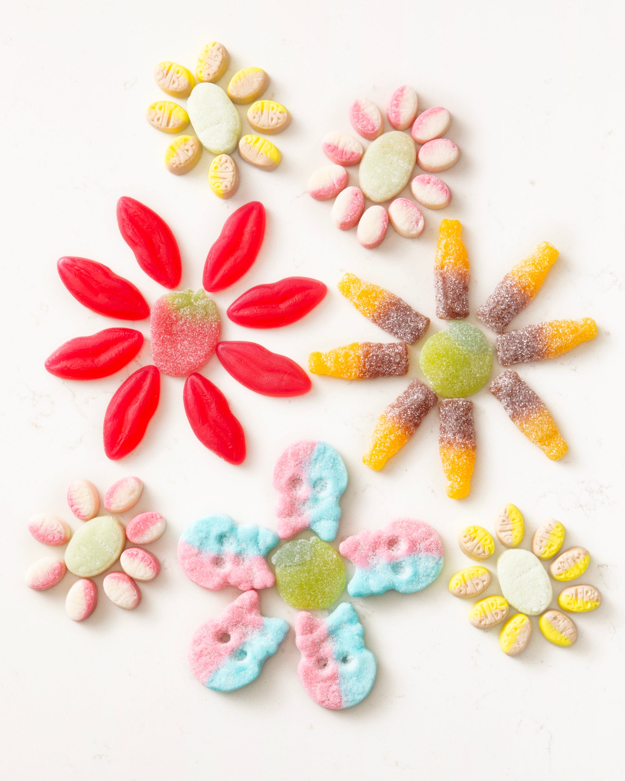 Colorful gummy candies arranged in flower shapes on a white background with varying bright colors.