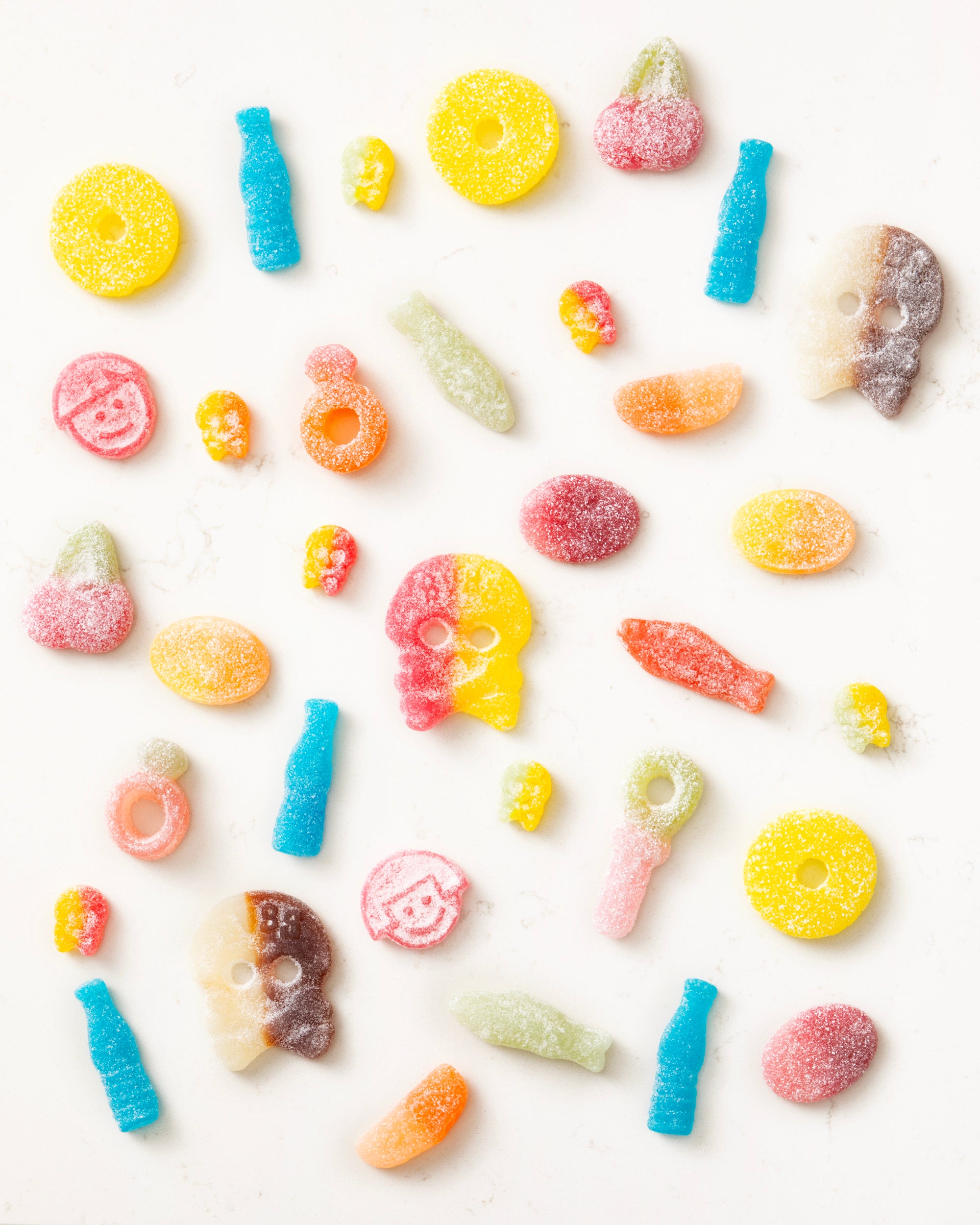 Colorful assorted vegan gummy candies including skulls, bottles, rings, and fruit shapes coated with sugar crystals