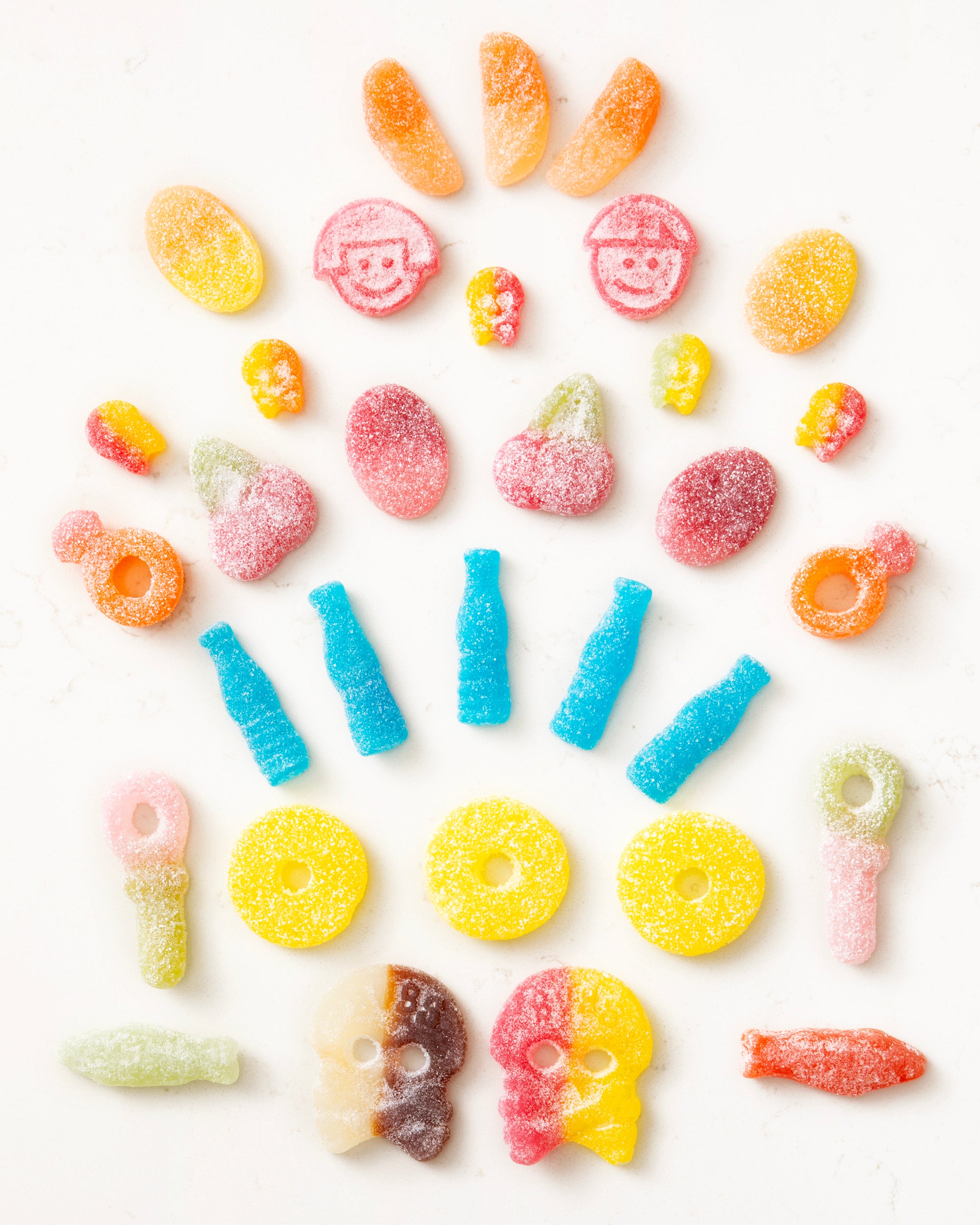 Assorted colorful sugar-coated gummy candies arranged by shape and color on a white background